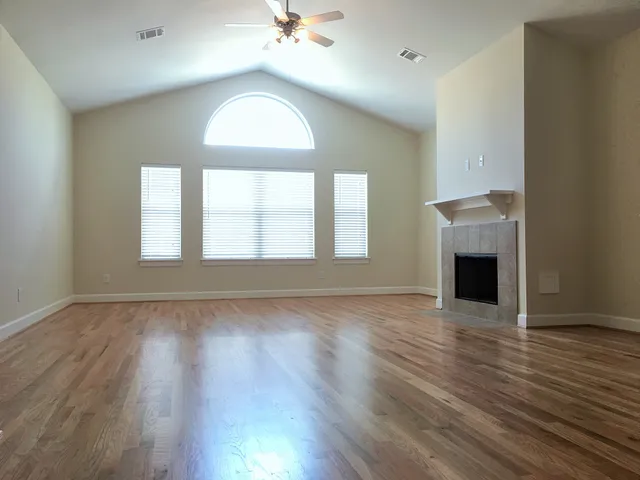 an empty room with wooden floor fireplace and windows