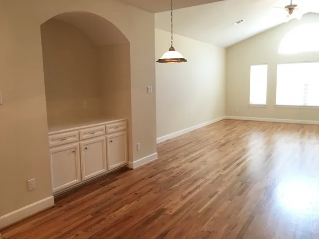 an empty room with wooden floor cabinet and windows