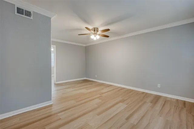a view of an empty room with wooden floor and a ceiling fan