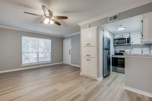 a view of an empty room with kitchen view and wooden floor
