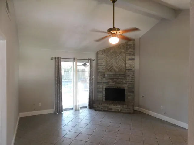 a view of an empty room with chandelier fan and fire place