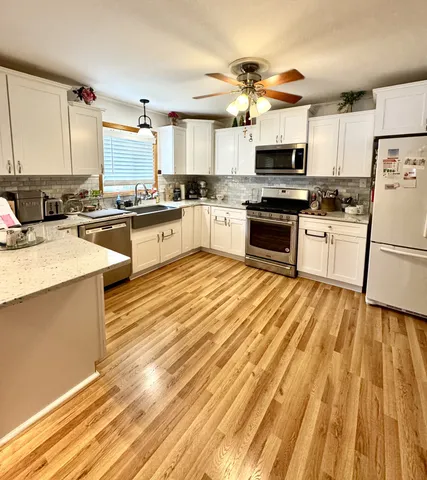 a kitchen with granite countertop a stove top oven a sink dishwasher a refrigerator and white cabinets with wooden floor