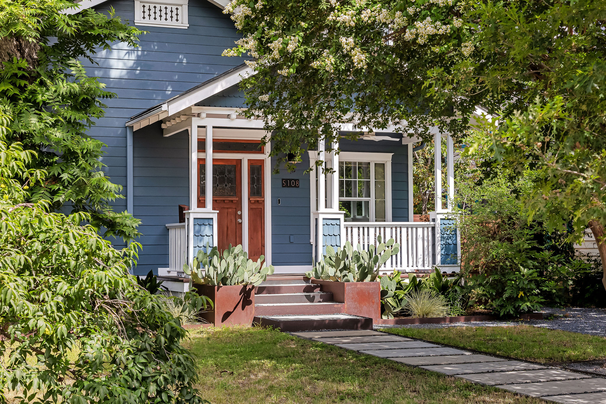 5108 Eilers Avenue Austin, TX 78751 - Photo 29 of 39 A charming blue craftsman home features a welcoming front porch framed by mature trees and desert landscaping.