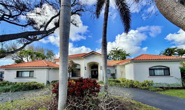 a white house with a flower garden and a large tree
