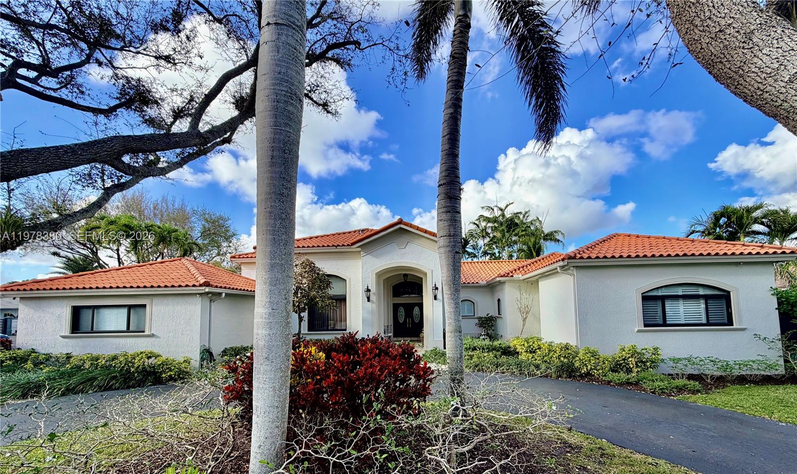 a white house with a flower garden and a large tree
