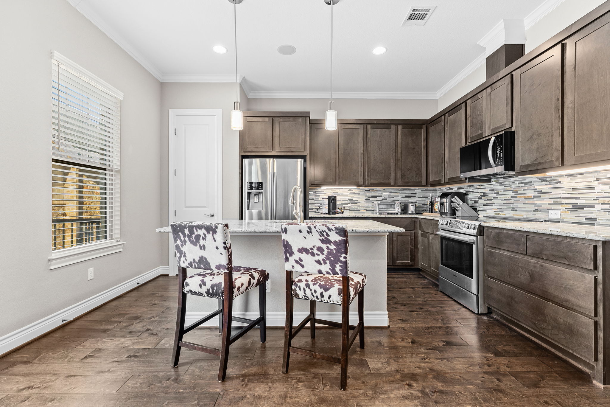 1125 Highknoll Lane Georgetown, TX 78628 - Photo 8 of 40 Kitchen with stainless steel appliances, an island with sink, light stone counters, decorative light fixtures, and dark wood finish cabinetry