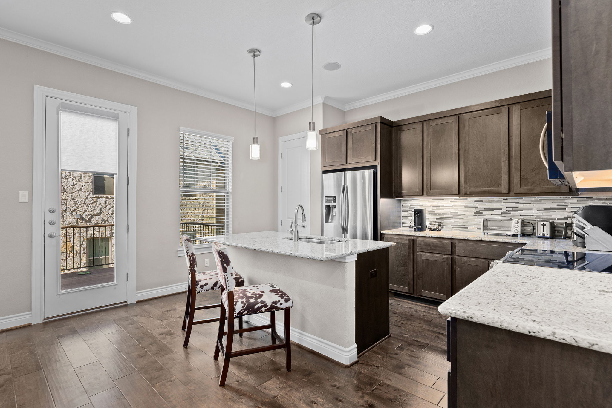 1125 Highknoll Lane Georgetown, TX 78628 - Photo 9 of 40 Kitchen featuring light stone counters, a center island with sink, dark wood finish cabinets, stainless steel fridge with ice dispenser, and crown molding