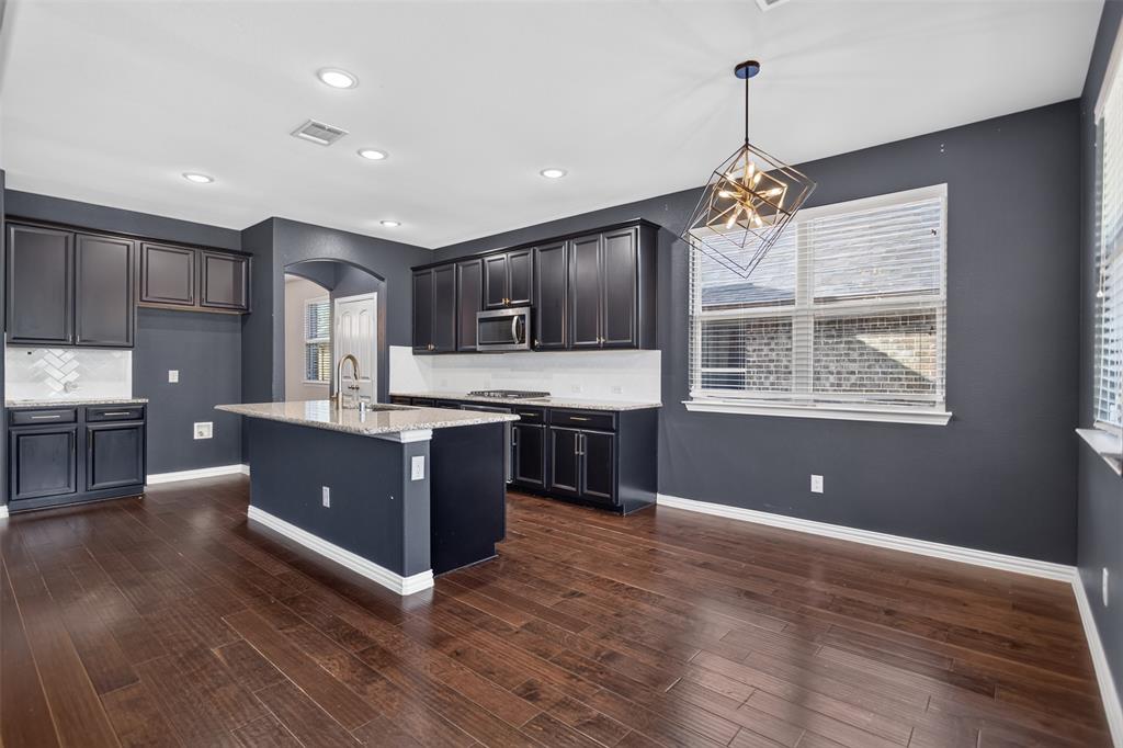 2066 Avondown Road Forney, TX 75126 - Photo 12 of 33 Spacious kitchen featuring an expansive center island with a chrome gooseneck faucet, dark wood-finish flooring, recessed lighting, and a contemporary geometric chandelier