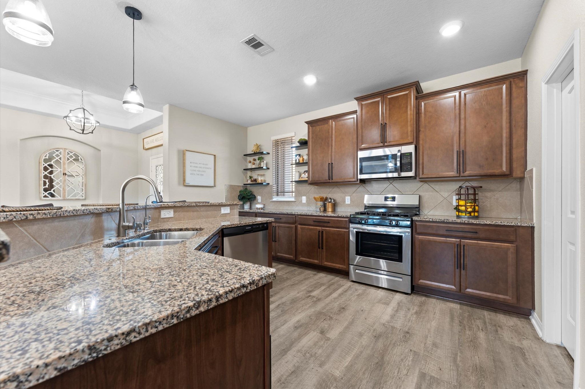 9729 Hidalgo Street Conroe, TX 77303 - Photo 18 of 38 Modern stainless steel appliances, granite countertops, and rich wooden cabinetry. It's well-lit with pendant and recessed lighting, complemented by a sleek faucet and open shelving for a contemporary touch.