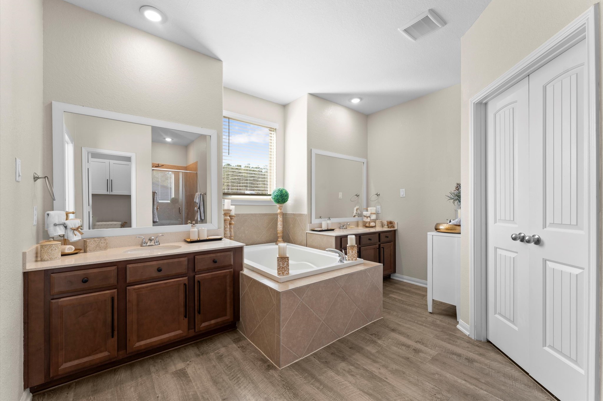 9729 Hidalgo Street Conroe, TX 77303 - Photo 21 of 38 The primary en-suite bath features a spacious, modern design with dual sinks, large mirrors, and a soaking tub. It has warm wood cabinetry, elegant fixtures, and a separate shower, all complemented by natural light and stylish flooring.