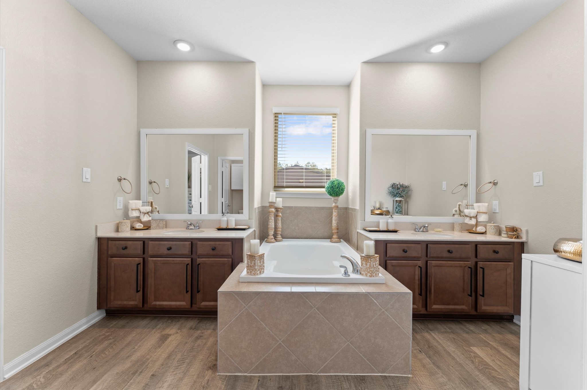 9729 Hidalgo Street Conroe, TX 77303 - Photo 23 of 38 Another view on the primary bath showcasing the spacious layout with dual sinks, elegant wood cabinetry, and a central bathtub. Natural light pours in through the window, highlighting the neutral tones and sleek fixtures, creating a serene and inviting space.