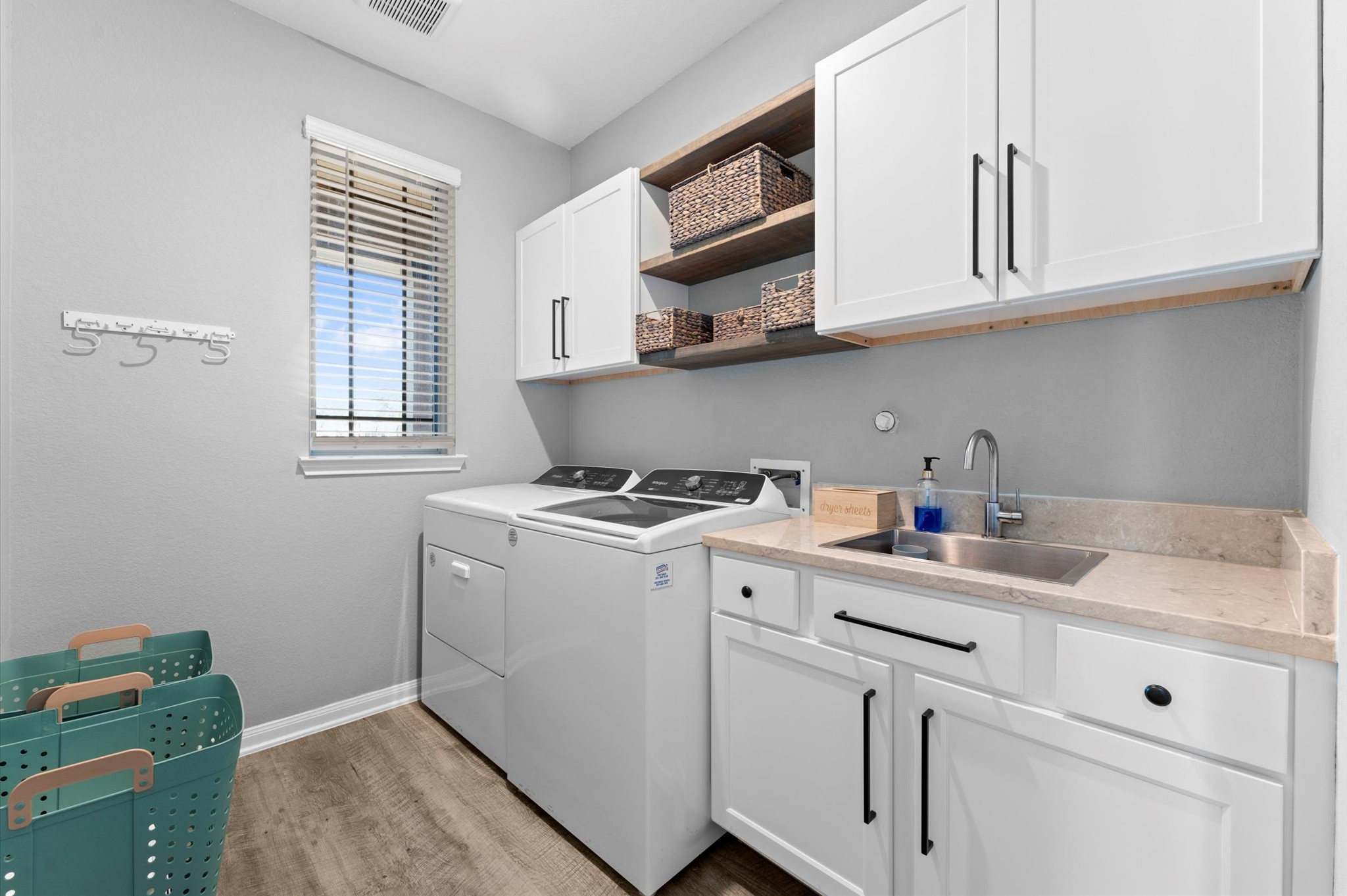 9729 Hidalgo Street Conroe, TX 77303 - Photo 29 of 38 Modern laundry room recently remodeled and features sleek white cabinetry, and a countertop with a sink. There's ample storage with open shelving and a window providing natural light. The space is well-organized and functional.