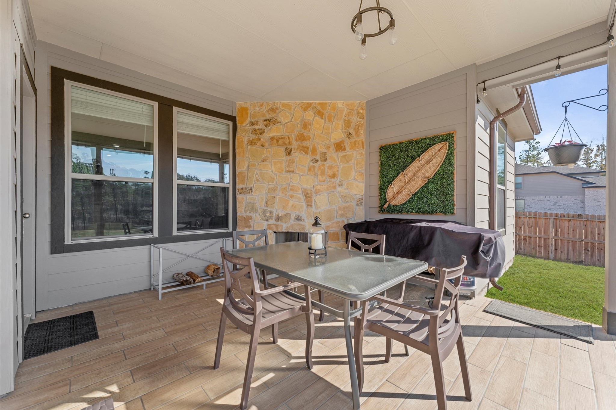 9729 Hidalgo Street Conroe, TX 77303 - Photo 30 of 38 Cozy outdoor covered patio with a corner stone fireplace and tiled flooring. It overlooks the fully fenced large backyard, offering a perfect spot for outdoor dining and relaxation.