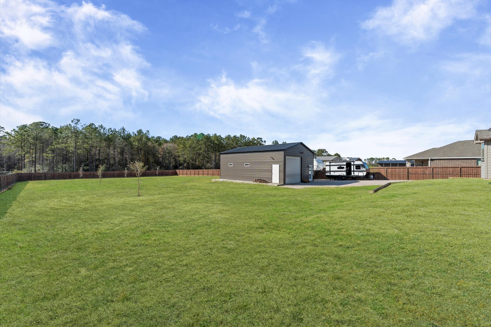 9729 Hidalgo Street Conroe, TX 77303 - Photo 33 of 38 Expansive backyard with large shop that includes an office as well as 50-amp RV hookup + 240V connection. The area is behind the custom gate and fencing, providing privacy, and there's ample space for outdoor activities or future additions.