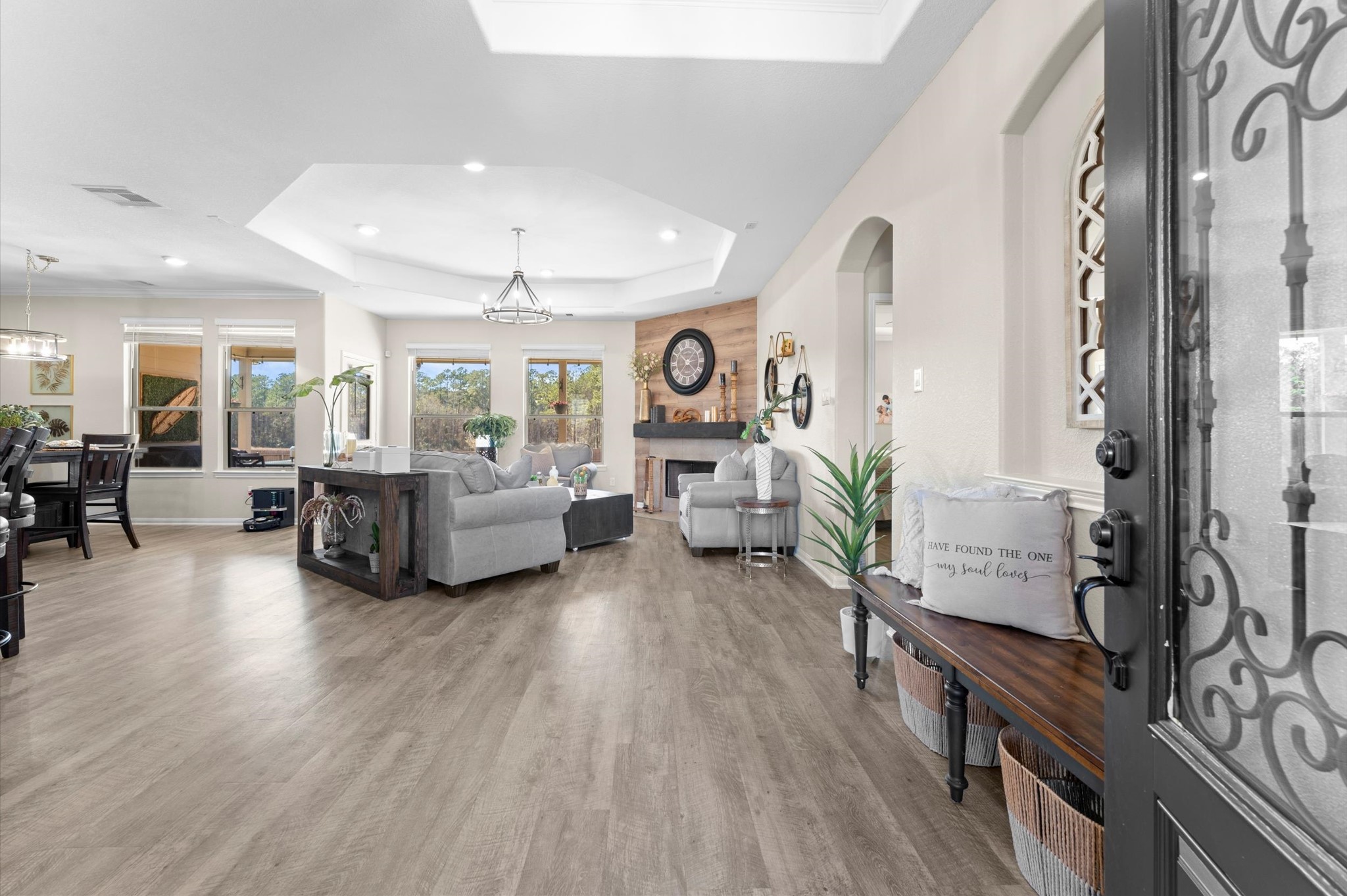 9729 Hidalgo Street Conroe, TX 77303 - Photo 7 of 38 Step inside to the spacious, open-concept living area with modern wood-look vinyl flooring and abundant natural light. It features a cozy seating area with trey ceiling, a contemporary fireplace with decorative wood accent. Large windows offer scenic views, and there's a seamless flow to the dining area, perfect for entertaining.