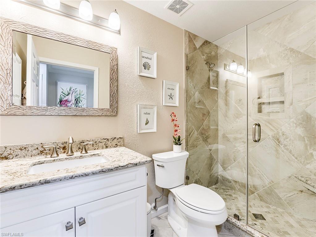 23011 Rosedale Drive, Unit 101 Estero, FL 34135 - Photo 28 of 34 a bathroom with a granite countertop toilet a sink and a mirror