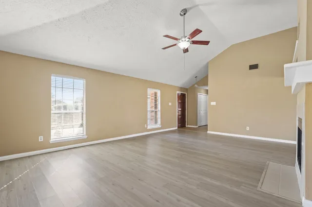 an empty room with wooden floor chandelier fan and windows