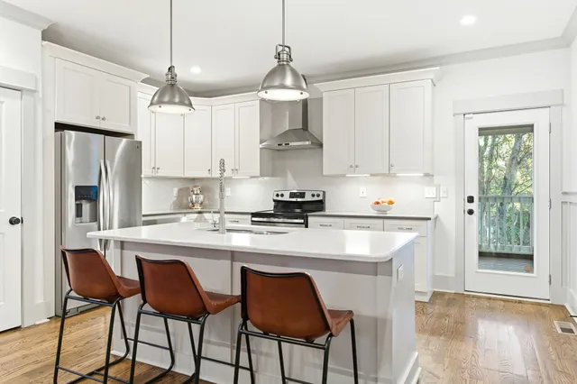 a kitchen with stainless steel appliances a stove a refrigerator a sink and white cabinets with wooden floor