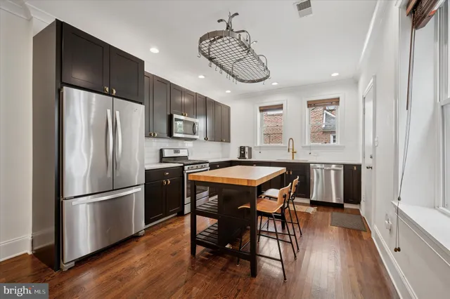 a kitchen with stainless steel appliances granite countertop a dining table chairs refrigerator and microwave