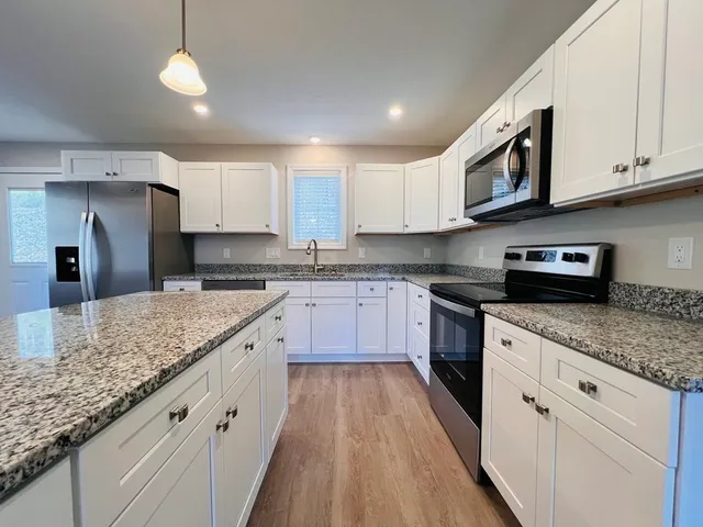 a large kitchen with granite countertop a sink a counter space stainless steel appliances and cabinets