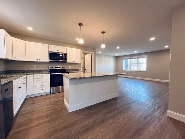 a large kitchen with kitchen island granite countertop a stove top oven a sink a counter space and cabinets