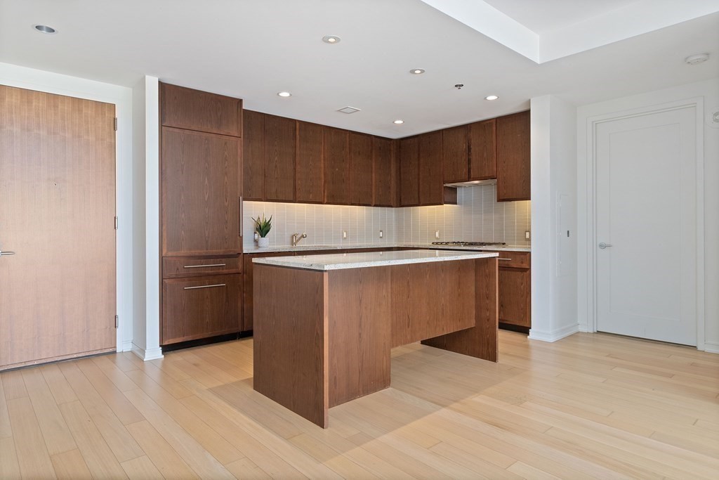 580 Washington Street, Unit 1207 Boston, MA 02111 - Photo 3 of 16 a kitchen with kitchen island granite countertop wooden cabinets and white appliances