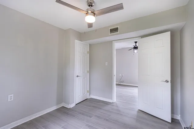 an empty room with wooden floor fan and windows
