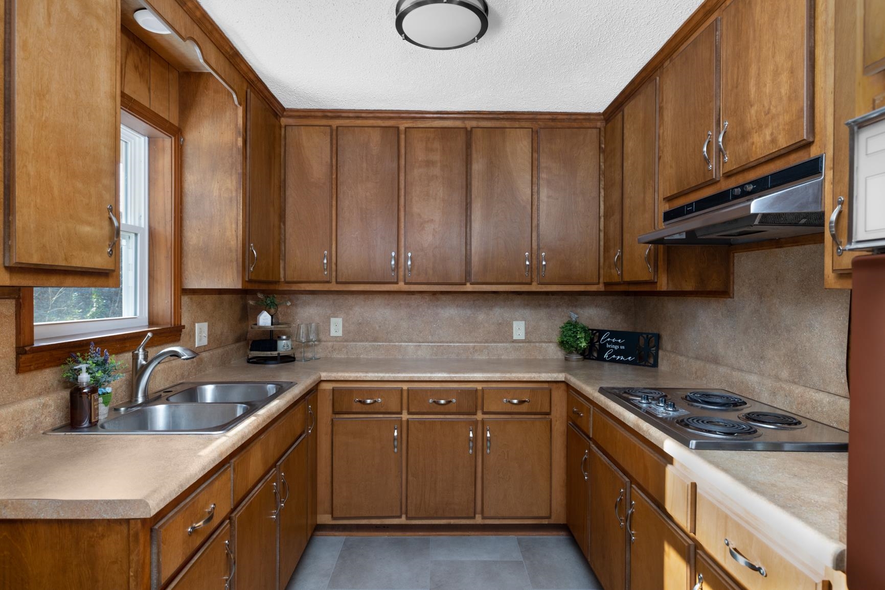 945 Gay Road Burlison, TN 38015 - Photo 16 of 27 Kitchen featuring under cabinet range hood, light countertops, stainless steel electric cooktop, brown cabinets, and a textured ceiling