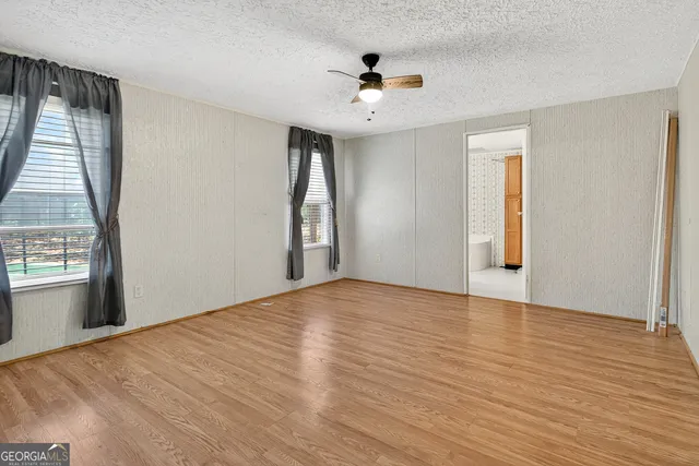 a view of an empty room with wooden floor and a ceiling fan