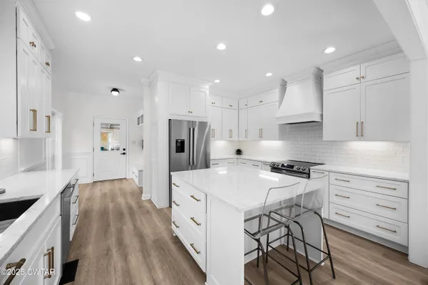 a kitchen with stainless steel appliances a stove a sink a refrigerator and white cabinets with wooden floor