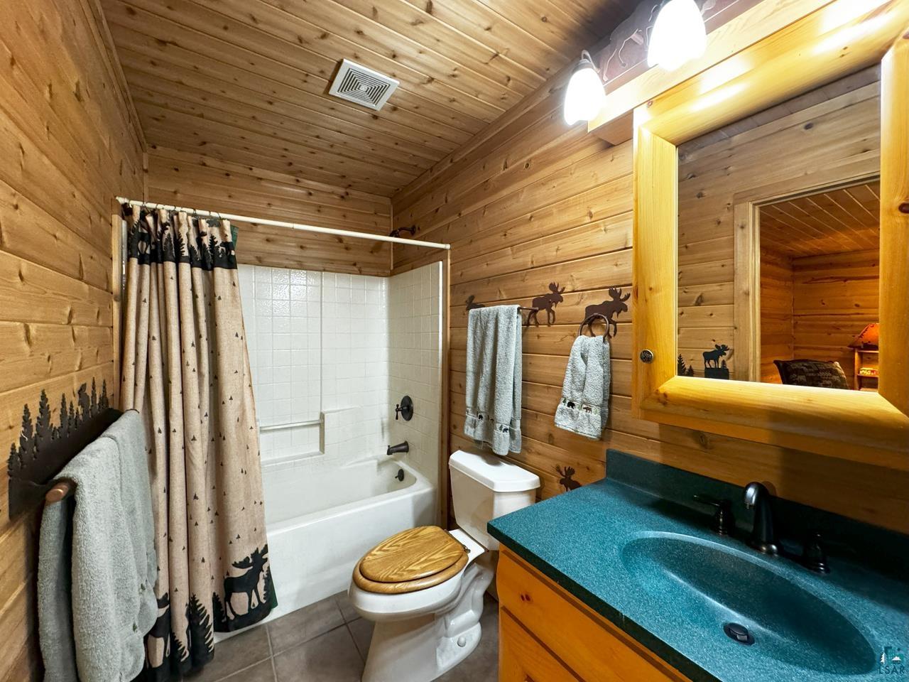 7236 Far North Road Orr, MN 55771 - Photo 27 of 42 Bathroom featuring wood walls, tile patterned floors, toilet, shower / bath combo with shower curtain, and vanity