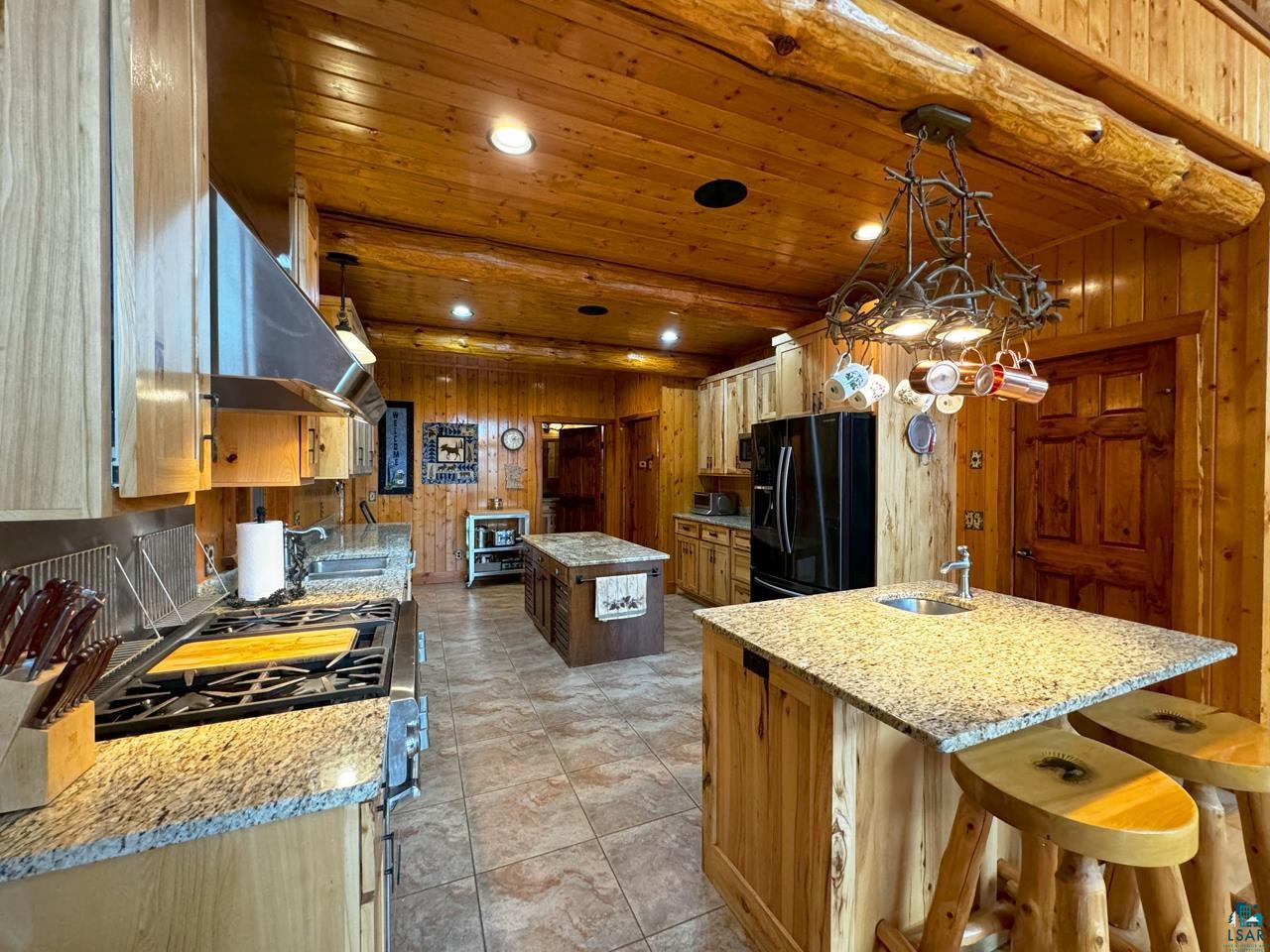 7236 Far North Road Orr, MN 55771 - Photo 8 of 42 Kitchen with black refrigerator with ice dispenser, a center island, extractor fan, stainless steel gas stove, and wood walls