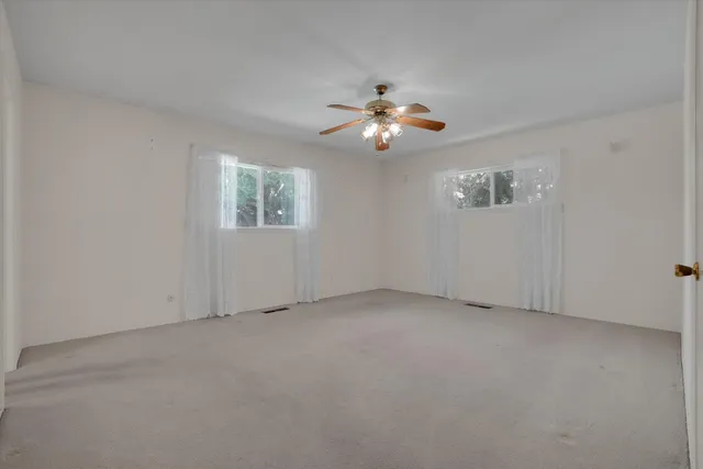 an empty room with windows and chandelier fan