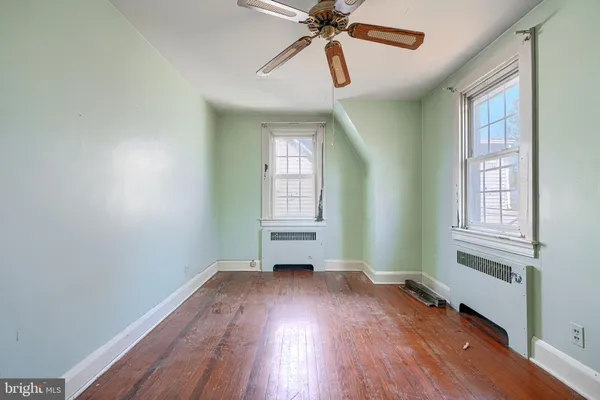 an empty room with wooden floor fan and windows