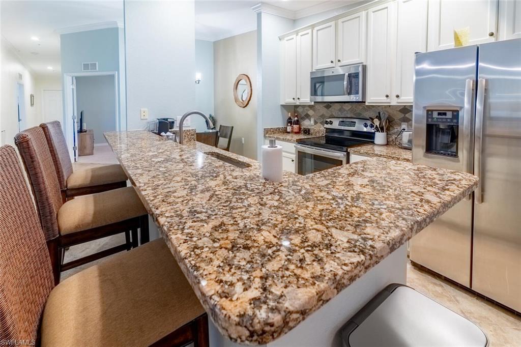 9828 Venezia Circle, Unit 1124 Naples, FL 34113 - Photo 11 of 50 a kitchen with stainless steel appliances kitchen island granite countertop a refrigerator oven a sink dishwasher and white cabinets with wooden floor