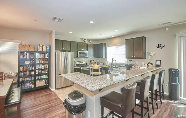 a kitchen with stainless steel appliances granite countertop a stove top oven a sink dishwasher and a refrigerator with wooden floor