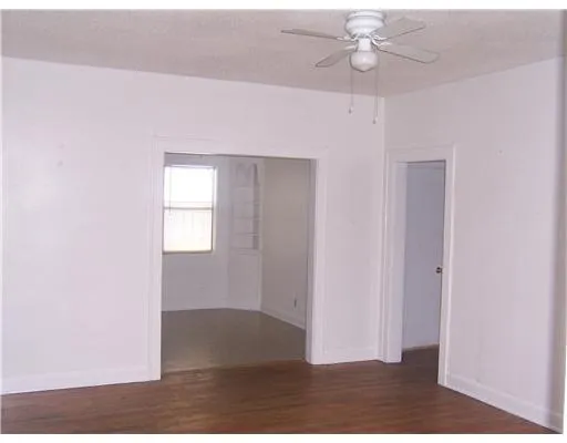 an empty room with wooden floor ceiling fan and windows