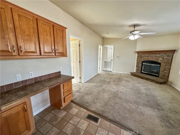 an empty room with chandelier fan and kitchen view
