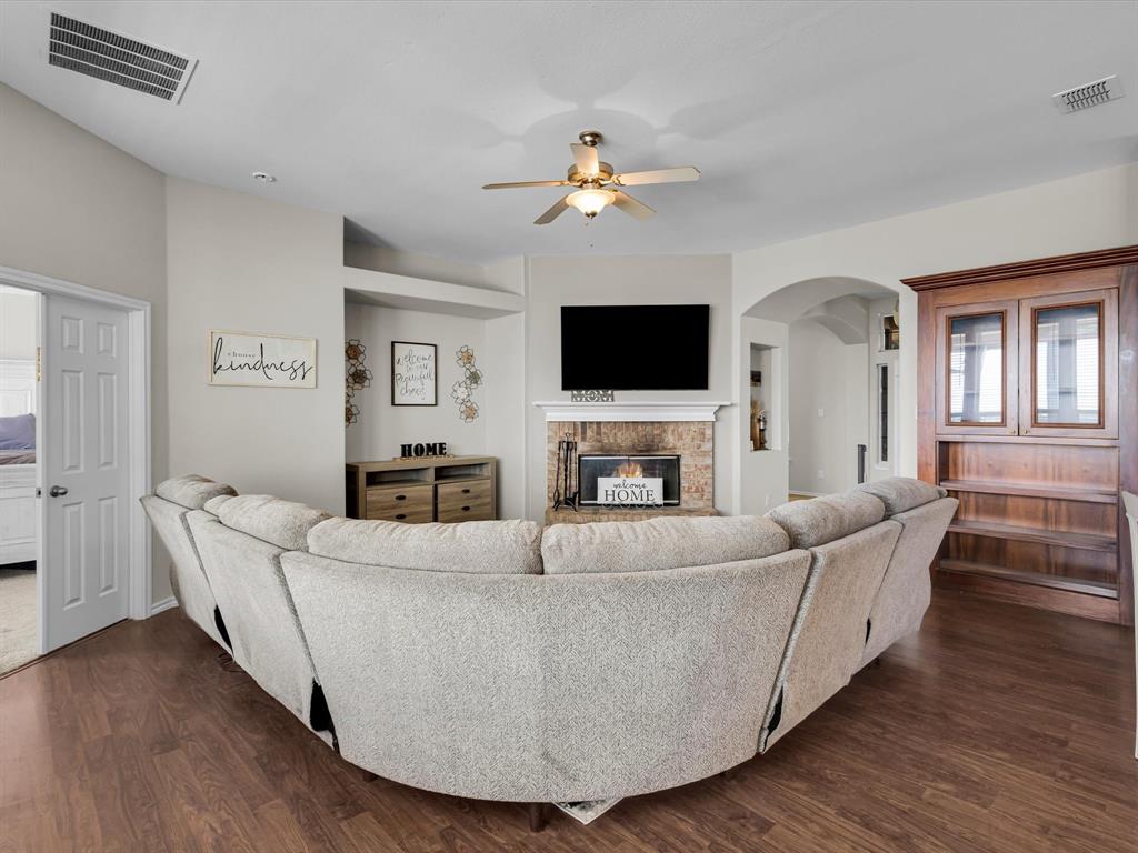 205 King George Road Ponder, TX 76259 - Photo 11 of 37 Wood-finish flooring throughout, ceiling fan with integrated lighting, built-in fireplace with stone surround, arched doorway, and a built-in wood-finish display cabinet