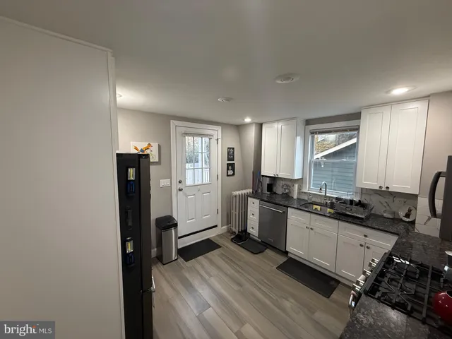 a kitchen with stainless steel appliances granite countertop a refrigerator a sink dishwasher a stove and white countertops with wooden floor