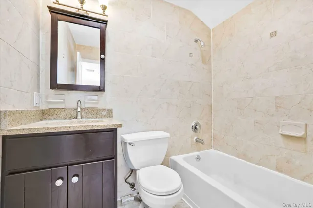 a bathroom with a granite countertop toilet a sink a mirror and bathtub
