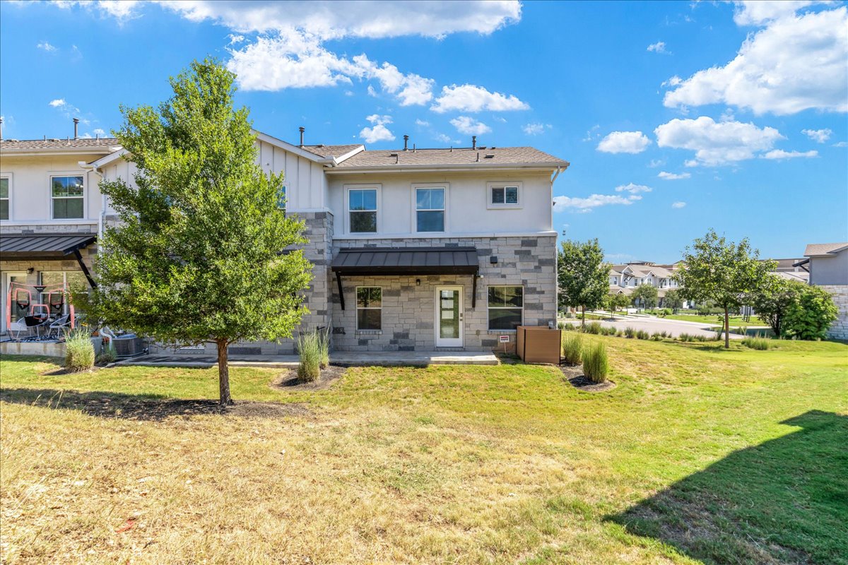 2021 Local Rebel Street, Unit 2021 Leander, TX 78641 - Photo 34 of 40 Back of house with stone siding, a patio area, a yard, a metal roof, and a standing seam roof