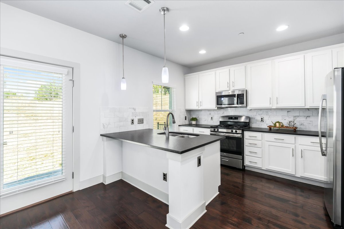 2021 Local Rebel Street, Unit 2021 Leander, TX 78641 - Photo 10 of 40 Kitchen featuring decorative backsplash, stainless steel appliances, dark wood-style flooring, decorative light fixtures, and white cabinets