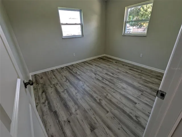 an empty room with wooden floor closet and windows