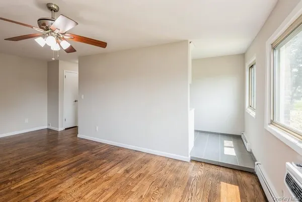 an empty room with wooden floor fan and windows