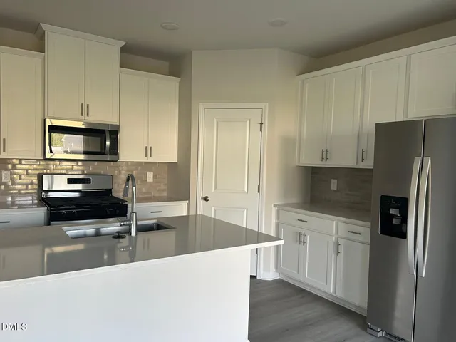 a kitchen with stainless steel appliances a refrigerator a sink a stove a microwave and white cabinets