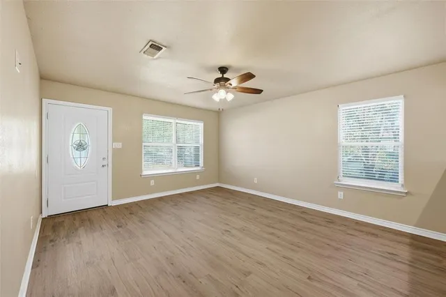 an empty room with wooden floor chandelier fan and windows