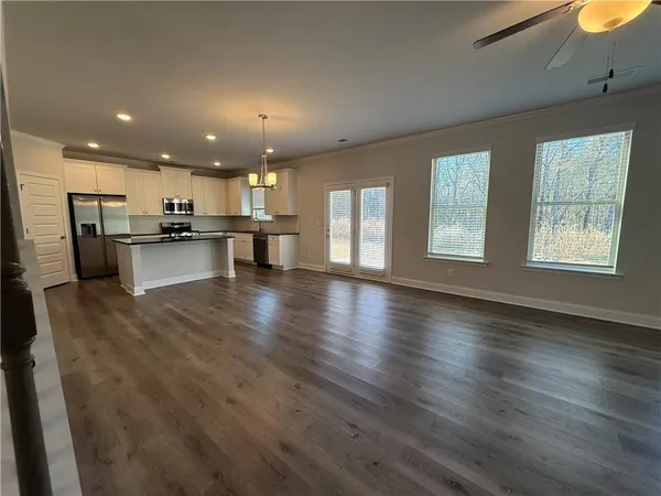 a open kitchen with stainless steel appliances kitchen island granite countertop a refrigerator a stove a sink dishwasher and white cabinets with wooden floor
