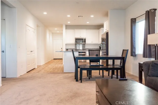 a living room with stainless steel appliances kitchen island granite countertop a table chairs and a refrigerator