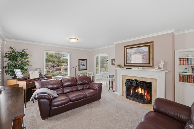 7576 South Jefferson Street Midvale, UT 84047 - Photo 9 of 53 Living space featuring a fireplace with a stone surround and white mantel, built-in shelving, crown molding, and carpeting